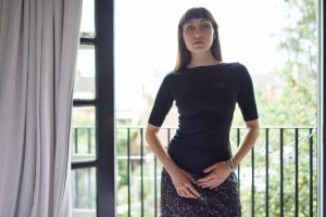 Model stood on a balcony wearing Cambridge Boat Neck and a gray skirt